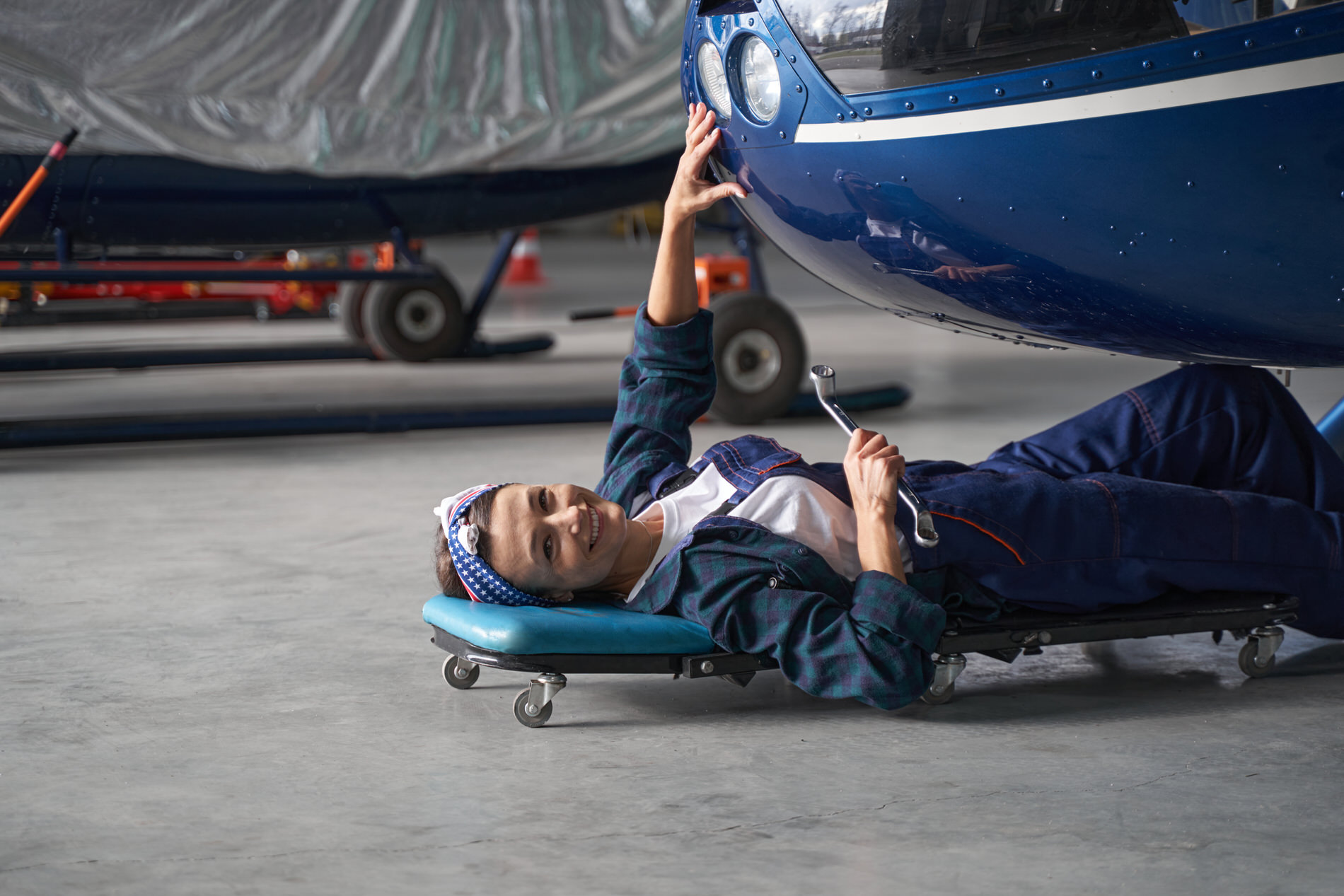 Eine Mechanikerin liegt unter einem Auto und lächelt